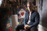 artist michael hermann sitting in front of his wall full of artwork