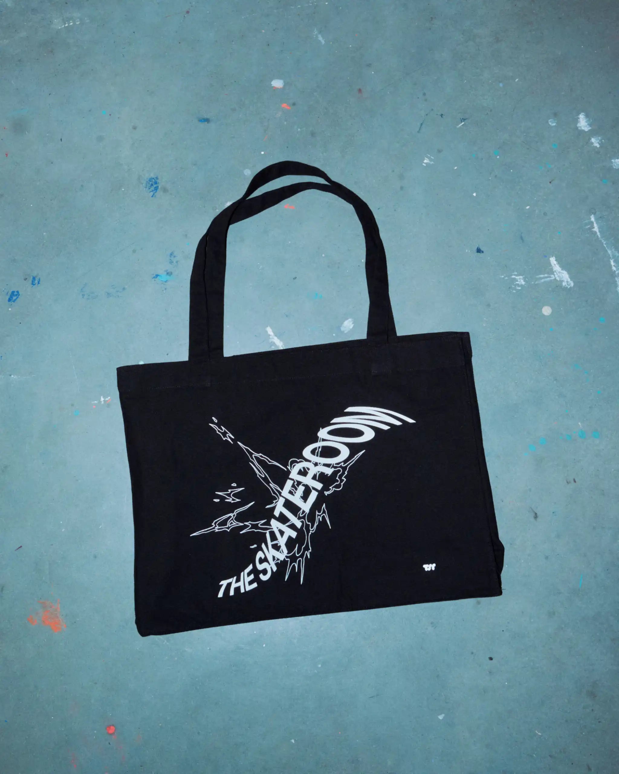 Minimalist black canvas tote bag with white print, styled against a concrete backdrop — sustainable design meets utilitarian streetwear.