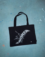Minimalist black canvas tote bag with white print, styled against a concrete backdrop — sustainable design meets utilitarian streetwear.