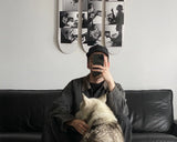 Person sitting on a couch with a dog, taking a mirror selfie in a room with a skate triptych by Ed Templeton on the wall.