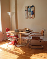 THE SKATEROOM’s “Charles the First” triptych by Jean-Michel Basquiat hangs above a modernist dining setup with a tulip table and a mix of vintage chairs. Warm sunlight casts shadows across the wooden floor, blending street art with interior elegance.