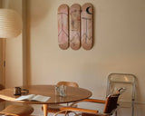 Dining area with a round table and chairs, featuring Both Poles skateboards by Jean-Michel Basquiat on the wall.