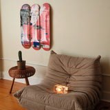 Three Jean-Michel Basquiat "Six Fifty" skate decks on a wall above a ligne-roset Togo sofa with a small wooden table and a cactus.