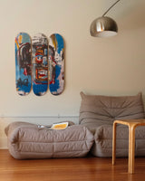Three Jean-Michel Basquiat "Skull" skate decks on a wall above two Togo sofas with a small wooden table in front.