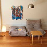 Three Jean-Michel Basquiat "Skull" skate decks on a wall above two Togo sofas with a small wooden table in front.