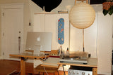 Interior home workspace featuring the ‘Blue Sky’ skateboard art edition by Wassily Kandinsky mounted on a white cabinet, styled alongside vintage Hi-Fi audio equipment, Macbook, record player, wooden speakers, and a minimalist paper lantern.