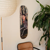 Frida Kahlo “The Wounded Deer” art skateboard by THE SKATEROOM, wall-mounted in a modern interior. Open edition skateboard deck featuring iconic surrealist painting, styled with rattan chair, leafy indoor plant, and paper lantern—perfect for art collectors, design lovers, and skateboard wall art enthusiasts.