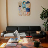 Jean-Michel Basquiat "Charles The First" triptych skateboard wall art by THE SKATEROOM, featuring three collectible decks mounted above a black leather sofa in a modern, minimalist living room. Styled with sculptural lighting and vintage decor—ideal for contemporary art and design collectors.