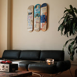 Jean-Michel Basquiat "Charles The First" triptych skateboard wall art by THE SKATEROOM, featuring three collectible decks mounted above a black leather sofa in a modern, minimalist living room. Styled with sculptural lighting and vintage decor—ideal for contemporary art and design collectors.