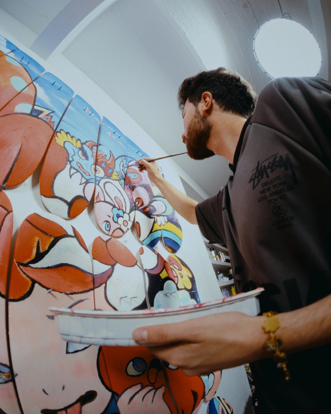 Close-up of artist VEXX painting fine details onto his ‘The Life of the Party’ mural across mounted skate decks in his studio.