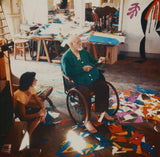 Henri Matisse in his studio, seated in a wheelchair, surrounded by colorful paper cut-outs, showcasing his creative process during his later years.