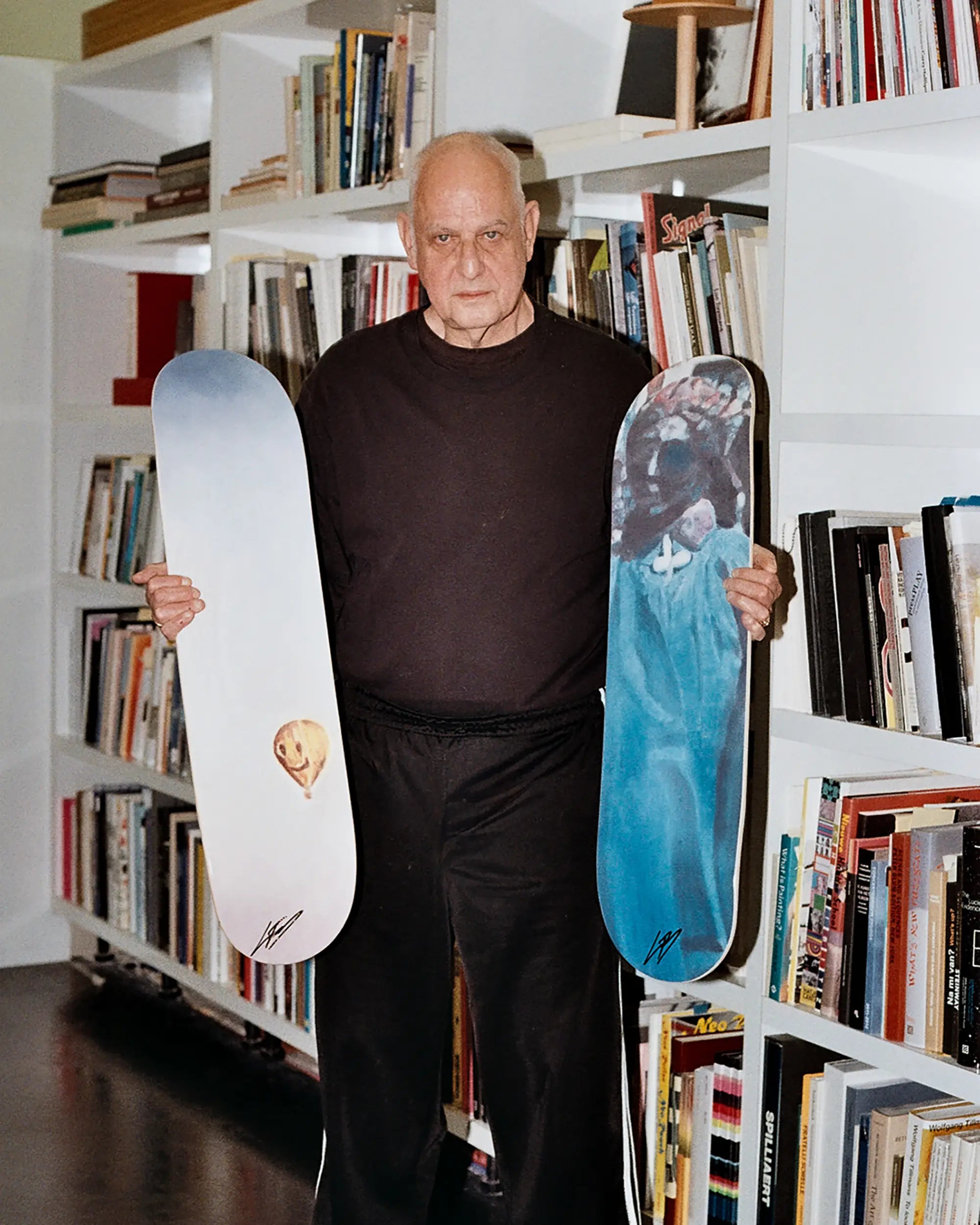 Belgian artist Luc Tuymans standing in front of a library with two skate decks of his art collection with THE SKATEROOM.
