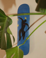 Close-up of the Henri Matisse 'Icare - Plate 8 of Jazz' skate deck, beautifully framed by lush green monstera leaves, highlighting its striking design and vibrant colors.