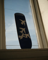 Henri Matisse 'Jazz' skate deck featuring white bird silhouettes on a deep blue background, beautifully displayed against a window with a clear sky backdrop.