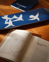 Henri Matisse 'Jazz' skate deck with white bird silhouettes displayed alongside an open art book and Matisse monograph, capturing a warm and creative atmosphere on a wooden floor.