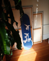 Henri Matisse 'Jazz' skate deck leaning against blank canvases, illuminated by soft natural light, with leafy plants framing the scene on a wooden floor.