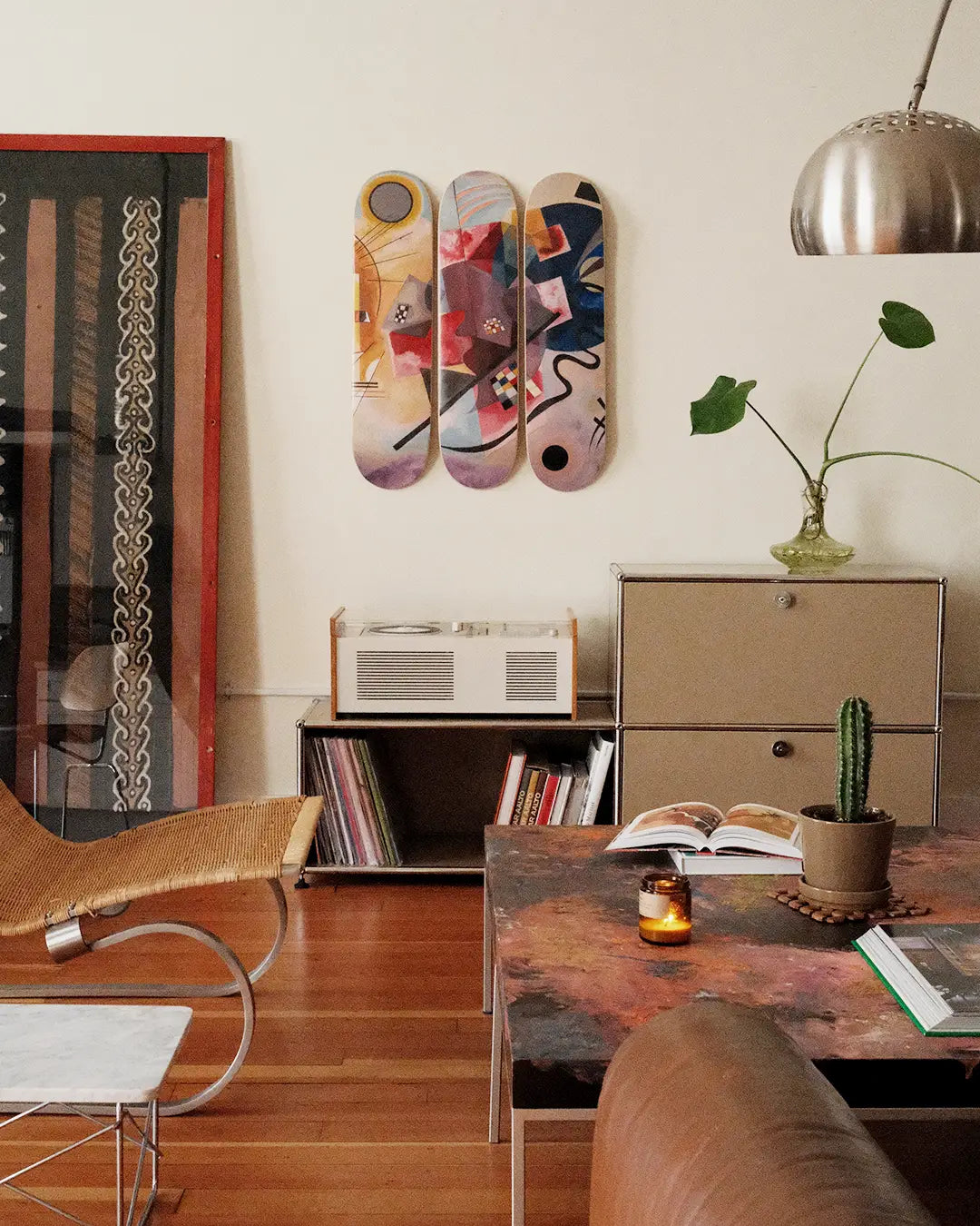 Modern living room with decorative skateboard decks by Wassily Kandinsky on the wall, a table with books and a plant, and a chair.