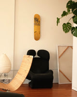 In a softly lit corner, THE SKATEROOM’s Untitled (New York) edition by Jean-Michel Basquiat hangs like a relic—graffiti-scrawled and defiant, in bold yellow against a muted wall. Beneath it, a sculptural black armchair and rattan chaise form a clash of textures: brutalism meets ease. A paper lantern, unframed canvas, and lush monstera leaves round out the scene, evoking the creative quiet of a lived-in studio. It’s a portrait of presence—art not as object, but as atmosphere.