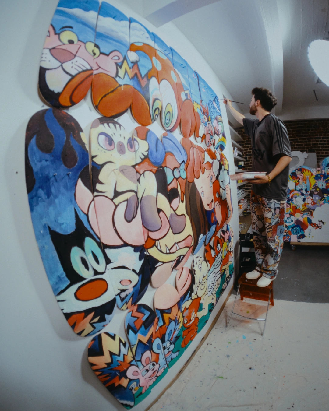 Artist VEXX hand-painting his large-scale mural ‘The Life of the Party’ directly onto 27 assembled skate decks in his studio.