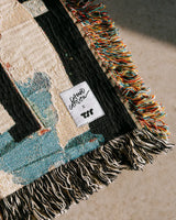 Multicolored woven blanket with a brand label saying David Carson x TSR on a neutral background