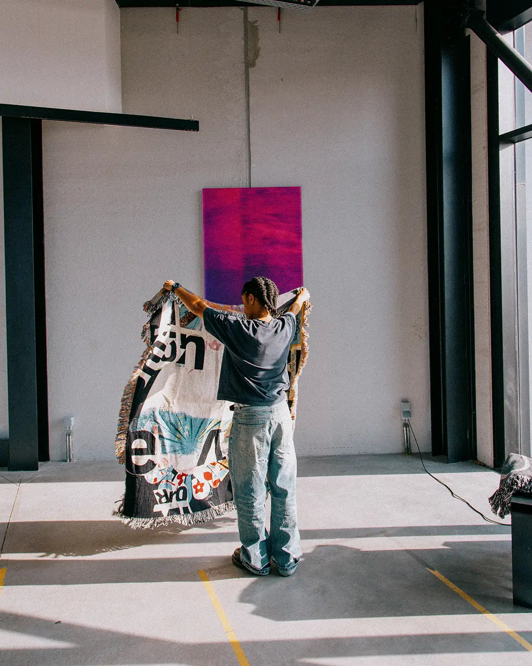 Person holding a woven blanket by artist David Carson in an indoor setting with a vibrant abstract painting on the wall.