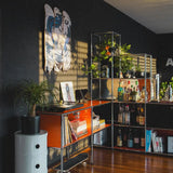 Modern interior featuring THE SKATEROOM’s Roy Lichtenstein 'Drowning Girl' skateboard triptych displayed as wall art, surrounded by plants, books, and a bar setup, showcasing a stylish and artistic living space.