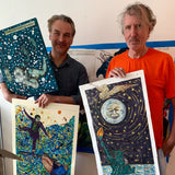 Artists Marcel Dzama and Raymond Pettibon holding up their collaborative artworks in a studio. The pieces feature surreal and expressive imagery, blending Dzama’s whimsical figures with Pettibon’s bold, narrative-driven style. This collaboration is part of their limited-edition collection with THE SKATEROOM.