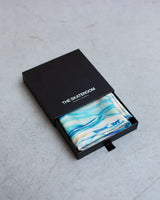 Blue patterned scarf in a black box with 'The Skateroom' branding on a gray surface.