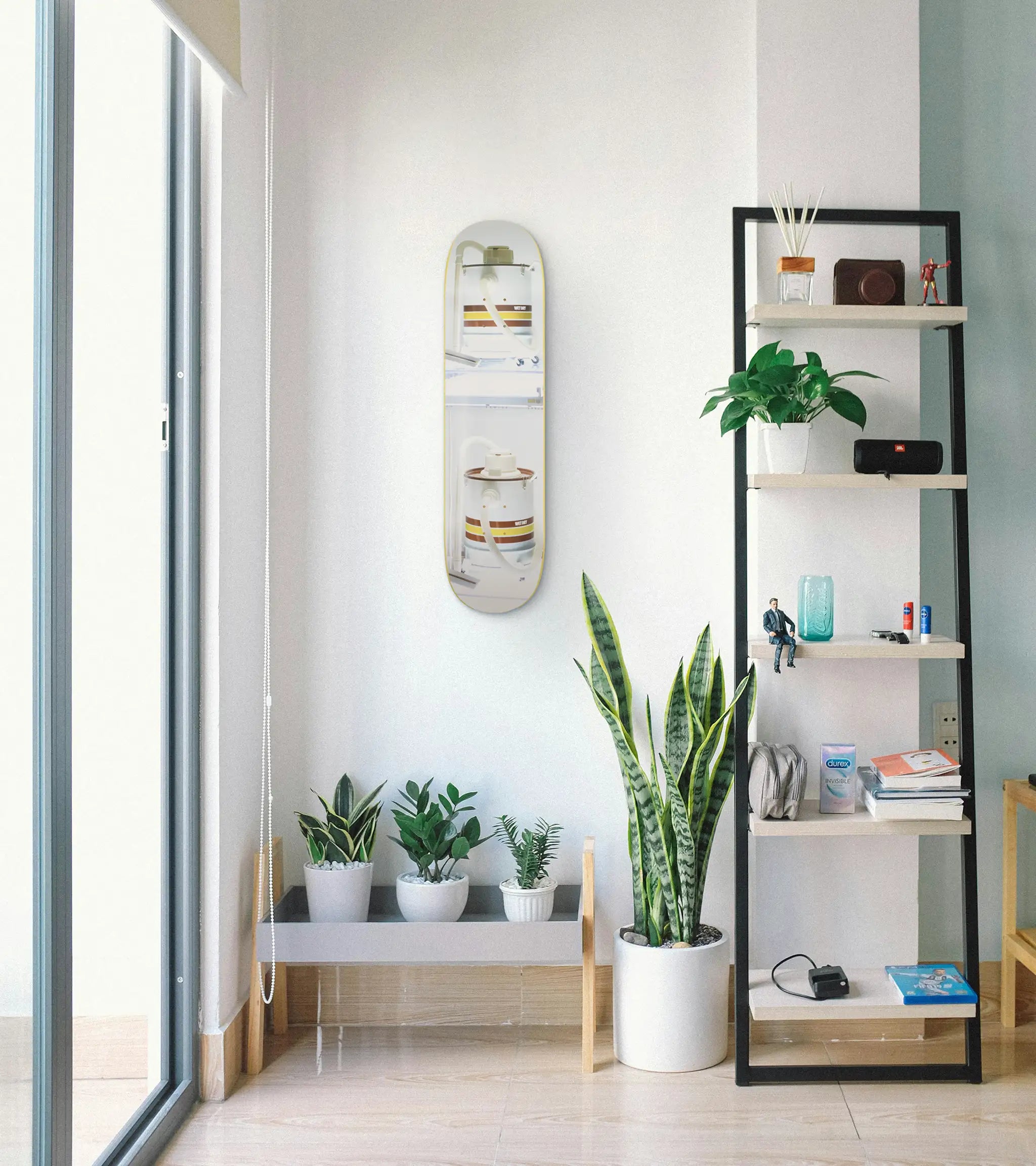 Modern interior with a shelf, mirror, and potted plants, and the Doubledecker Skateboard by Jeff Koons on the wall.