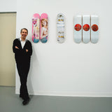 Jeff Koons standing next to his limited skateboard art editions by THE SKATEROOM featuring 'Pink Panther', 'Three Ball 50/50 Tank (Two Spalding Dr. J Silver Series, Wilson Supershot)' and 'New Shelton Wet/Dry 10 Gallon Doubledecker' designs.