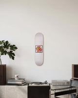 Skateboard deck with a Keith Haring design on a white wall above a brutalist credenza with design books and a plant.