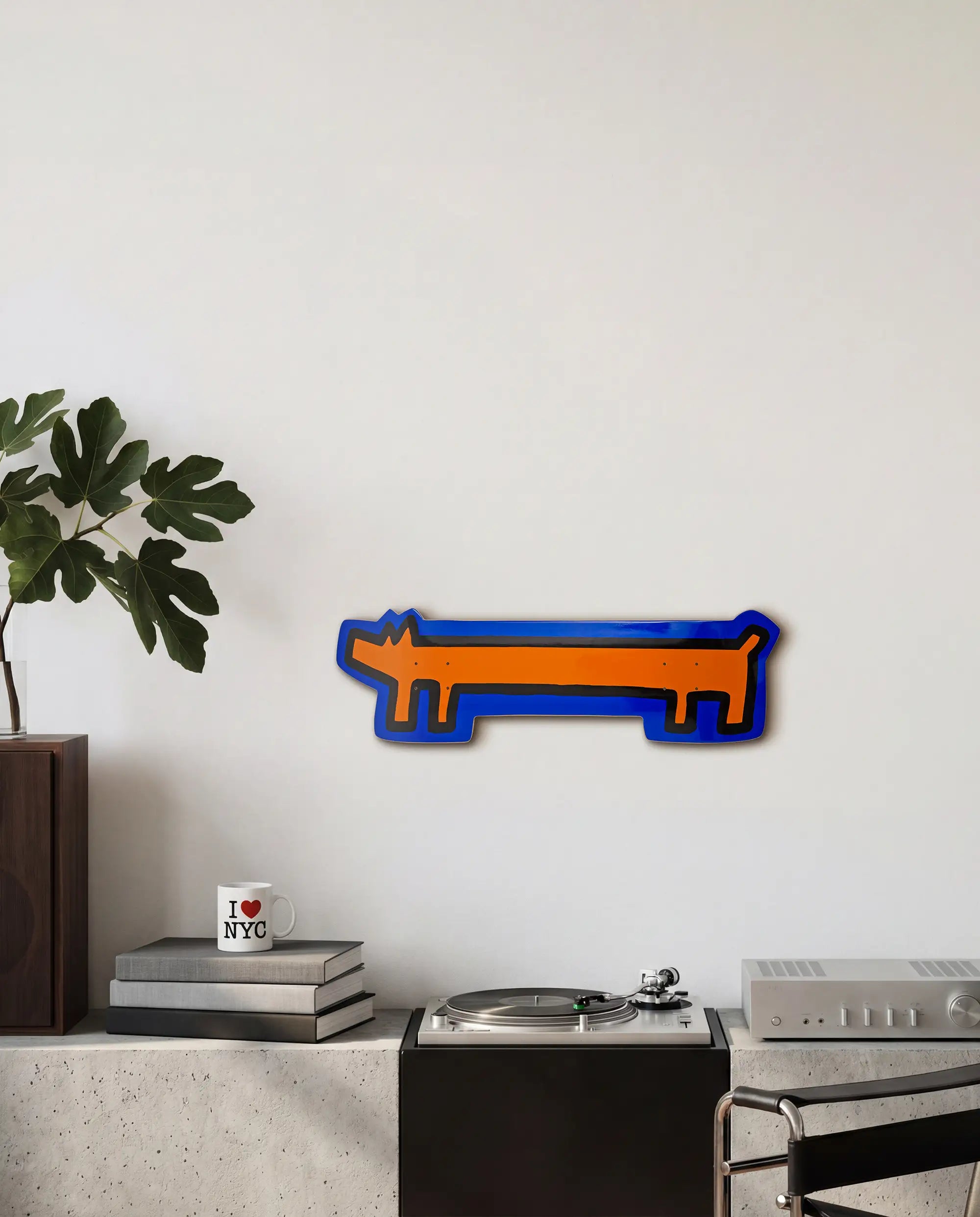 Decorative skateboard wall art of a blue and orange dog shape by Keith Haring on a white wall.