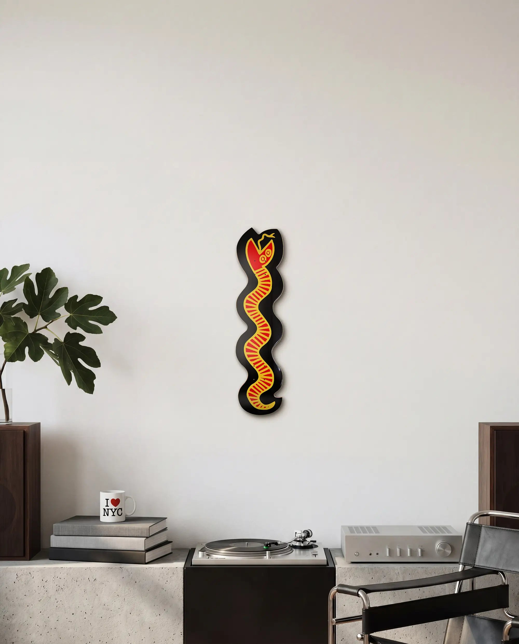 Decorative skateboard wall art in the shape of a snake by Keith Haring, on a white wall above a brutalist credenza.