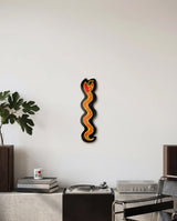 Decorative skateboard wall art in the shape of a snake by Keith Haring, on a white wall above a brutalist credenza.