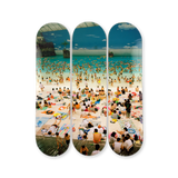 Three skateboard decks with a crowded beach scene photography by Martin Parr printed on them.