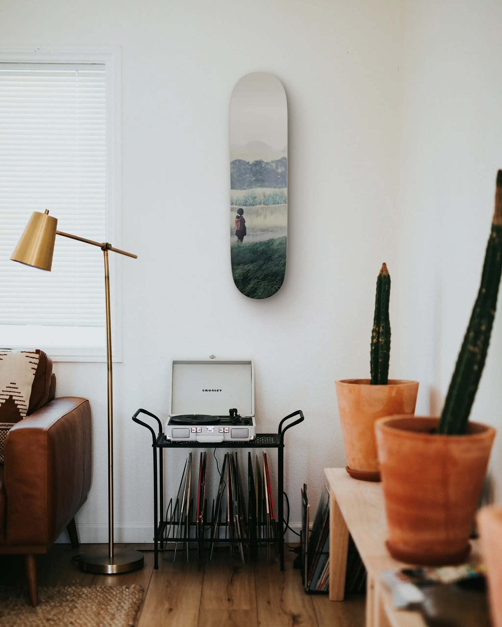 Living room with a Tomas Sanchez skateboard on the wall, a lamp, a couch, and potted plants.